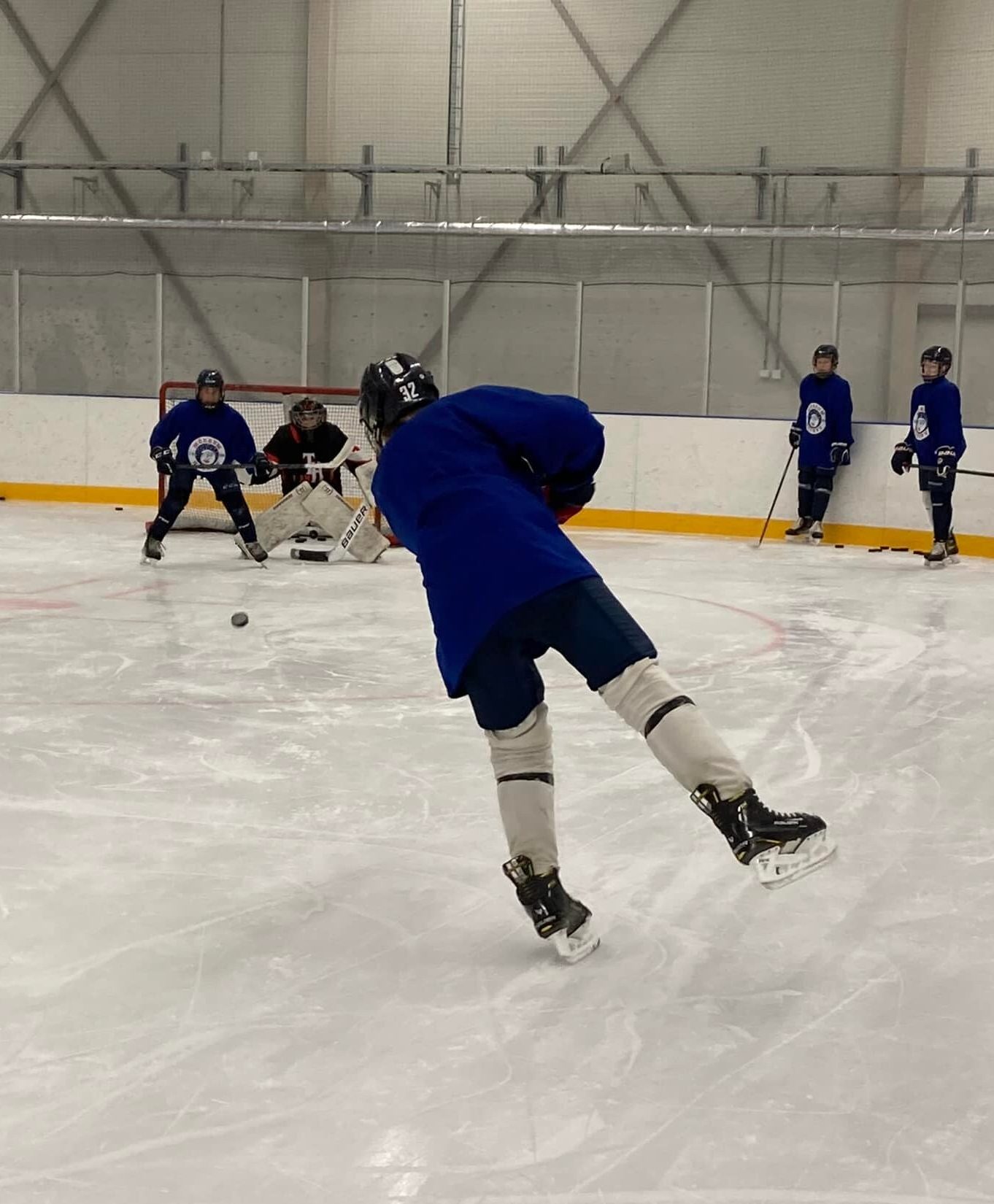 En ishockeyspelare i blå tröja åker mot målvakten och siktar på pucken under en träning i en ishall.